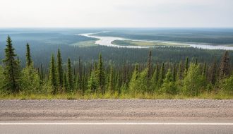 Wide road view into boreal wilderness of Wood Buffalo National Park from the Fort Smith gateway area, with a distant river and treeline.