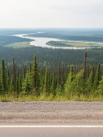 Wide road view into boreal wilderness of Wood Buffalo National Park from the Fort Smith gateway area, with a distant river and treeline.