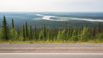 Wide road view into boreal wilderness of Wood Buffalo National Park from the Fort Smith gateway area, with a distant river and treeline.